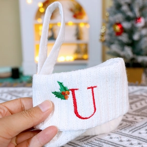 Close-up of white knitted Christmas stocking with red letter U embroidery and holly leaf