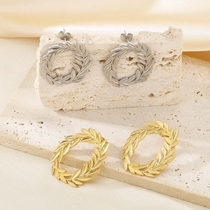 Elegant 18k gold and silver leaf wreath earrings displayed on stone with silk background