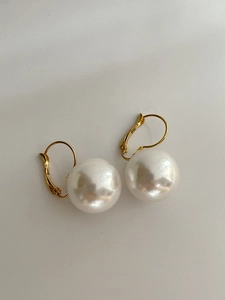 Detail view of round white resin pearls with 14K gold plated hooks on beige surface