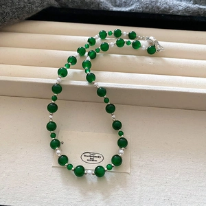 Détail de perles en verre vert émeraude avec accents blancs et fermoir argenté sur velours