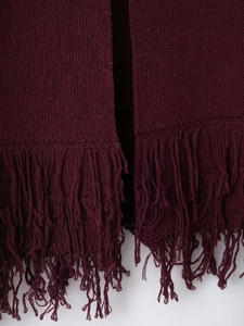 Detail of burgundy knit cardigan featuring long fringe tassels and fine knit texture