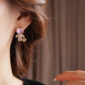 Close-up of a gold bear earring with pink gemstone and dangling heart on earlobe