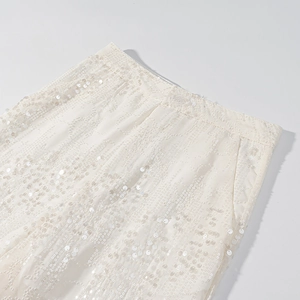 Dettaglio del ricamo di paillettes su pantaloni beige con finitura luccicante
