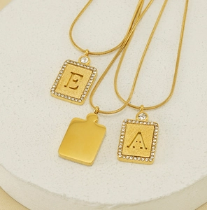 Detail von 18K vergoldeten rechteckigen Buchstabenanhängern mit Kristallen und Sandstrahleffekt