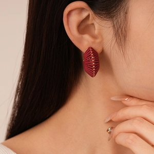 Close-up of a burgundy woven geometric stud earring with gold beads on model ear