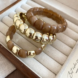 Close-up of gold chain bracelets and brown marble resin beads set on velvet background