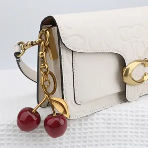 Close-up of white embossed leather bag with gold chain and red glitter cherry charm