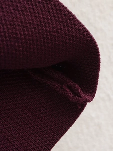 Detailopname van de bordeauxrode gebreide textuur met focus op de naden van het vest