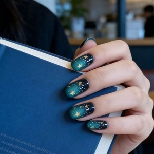 Gros plan sur les faux ongles avec dégradé vert foncé et motifs d'étoiles dorées