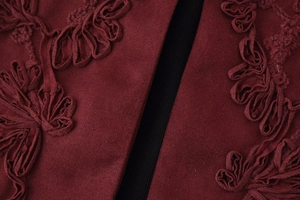 Detailed macro view of burgundy fabric with intricate 3D floral embroidery on the vest