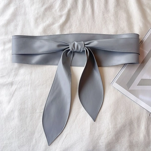 Détail d'une ceinture corset en cuir PU gris avec large nœud papillon sur tissu texturé