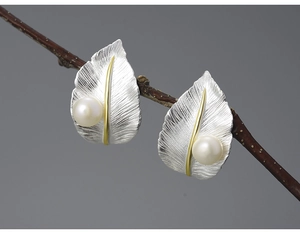 Macro view of silver and gold leaf earrings with white pearl on a branch