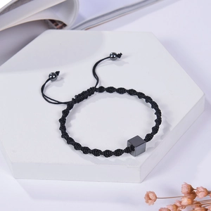 Detail of adjustable black braided bracelet with hematite cube on a stone display