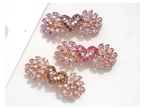 Dettaglio di fermagli per capelli con strass a cuore e ali in viola, rosa e marrone