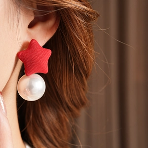 Detailed shot of red fabric star stud with a large white pearl drop earring on model