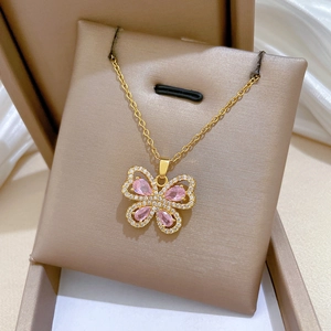 Macro detail of a golden necklace featuring a butterfly pendant with pink drop gemstones