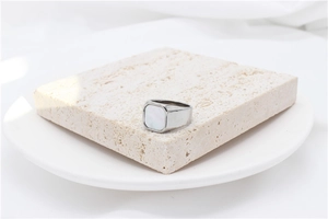 Close-up of a wide silver band ring with a square white shell inlay on a stone base