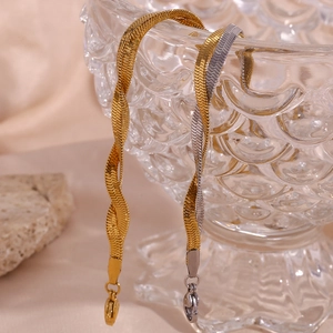 Detail of 18K gold plated braided blade chain anklets on textured glass bowl background