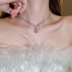 Close-up of a silver-toned necklace with a pink teardrop crystal pendant on a model