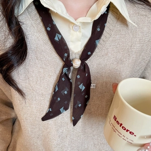 Close-up of a brown chiffon neck scarf with blue geometric patterns and a pearl buckle
