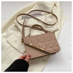 Close-up of beige quilted crossbody bag with gold metal buckle on a cream blazer background