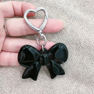 Elegant black acrylic bow keychain with heart hook held against beige knit background
