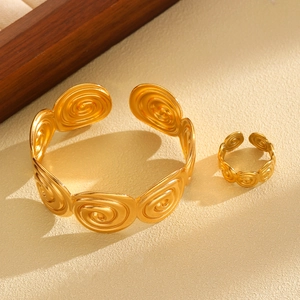 Macro shot of gold spiral textured disc details on the open cuff bracelet and ring set
