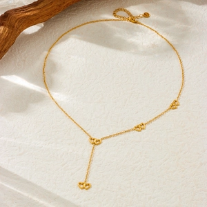 Detail of a gold double-heart pendant necklace with long tassel on a rustic wooden base