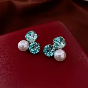 Silver needle earrings with light blue crystals and white pearls on red leather