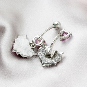 Macro shot of silver heart-shaped belly rings with purple zircon on pink silk fabric