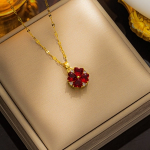 Golden clover necklace with red heart-shaped stones on a textured jewelry box