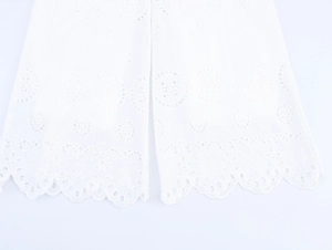 Close-up of white wide-leg trousers featuring hollow embroidery and a scalloped hem finish