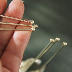 Macro detail of gold ball head pins for jewelry making held by hand to show fine texture