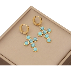 Elegant gold cross earrings featuring vibrant turquoise stones on a beige jewelry box
