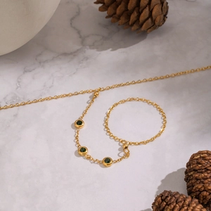 Detail of gold chain ring-bracelet with three green gemstones on marble surface