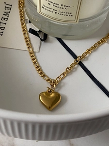 Detailed macro view of 18K gold-plated heart pendant and Figaro chain on ceramic