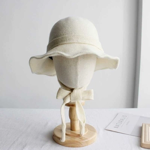 Cream knit bucket hat with decorative ribbon displayed on a wooden mannequin head