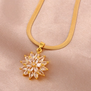 Macro shot of gold snake chain necklace with a crystal sunflower pendant on pink silk