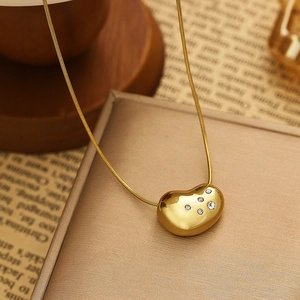 Macro shot of gold heart pendant with five crystals on a sleek snake chain necklace