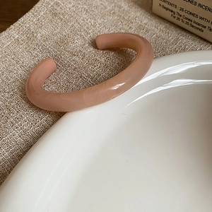 Detailed macro of pink marble resin open bangle resting on a ceramic bowl with warm lighting
