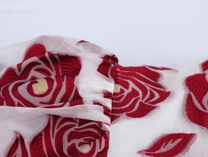Makroaufnahme roter Rosenstickerei auf weißem Netzstoff mit goldenen Akzenten