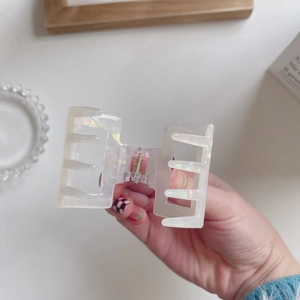Iridescent square acetate hair claw clip with metallic spring in hand close-up