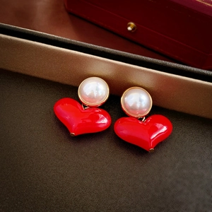 Macro shot of red heart stud earrings with white pearls on a textured leather surface