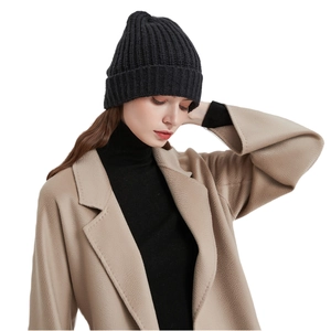 Classic black knitted beanie hat for winter, styled with a beige coat on a clean white background
