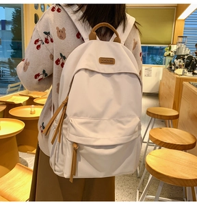 Detail of minimalist cream backpack showing the front pocket and leather fashion label