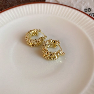 Detailed close-up of gold-toned textured hoop earrings on a decorative white ceramic plate