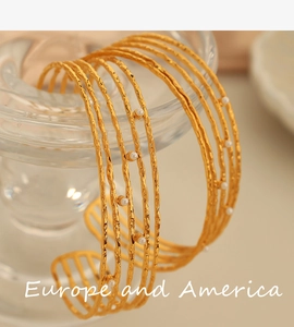Detail of layered gold open cuff bracelet with small white pearls on glass surface