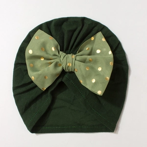 Close-up of baby turban hat in dark green featuring a large gold polka dot bow