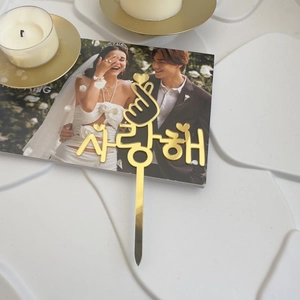 Close-up of golden acrylic love gesture cake topper with Korean I Love You engraving
