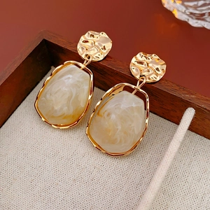 Macro detail of irregular gold-plated drop earrings with marble resin stone texture